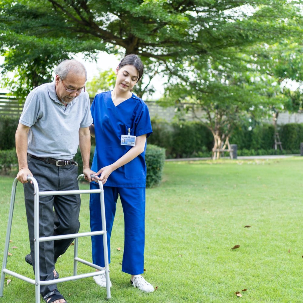 Asian young woman nurse at nursing home take care disabled senior man at backyard.