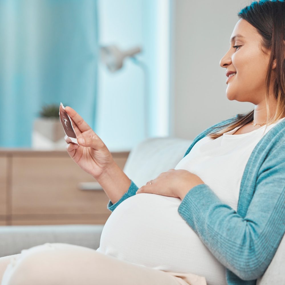 Pregnant, ultrasound and woman sitting on a sofa in the living room of her home with a baby bump or